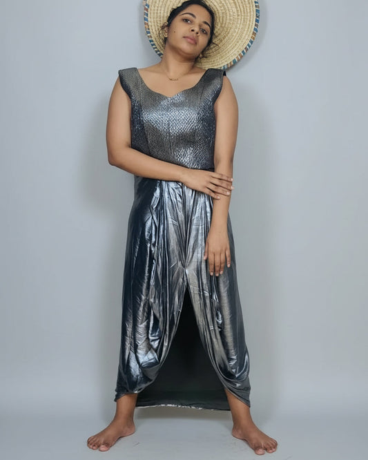 Woman wearing a metallic silver jumpsuit standing against a white wall with a plant and decorative items in the background.