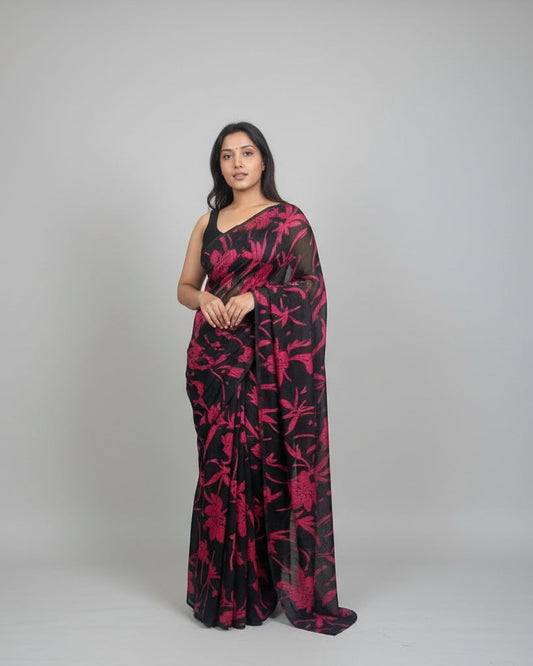 Woman wearing a black and red floral outfit standing in a room with decorative hats on the wall.