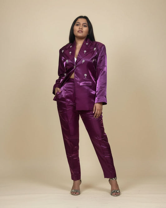 Woman in a shiny purple outfit standing in a room with a plant and decorative wall piece.