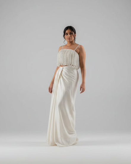 Woman wearing a white strapless top and flowing white skirt on a plain background