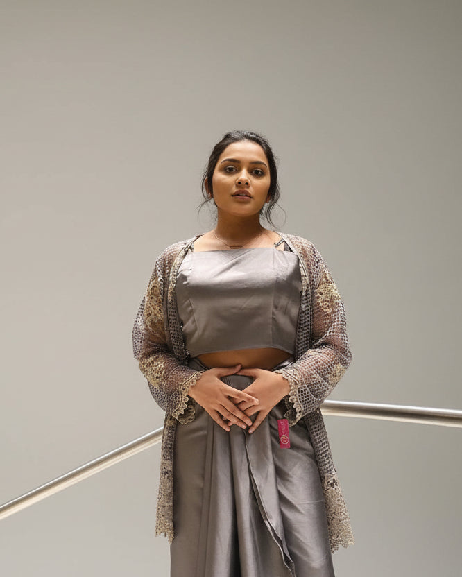 Woman in a gray outfit standing against a textured wall.