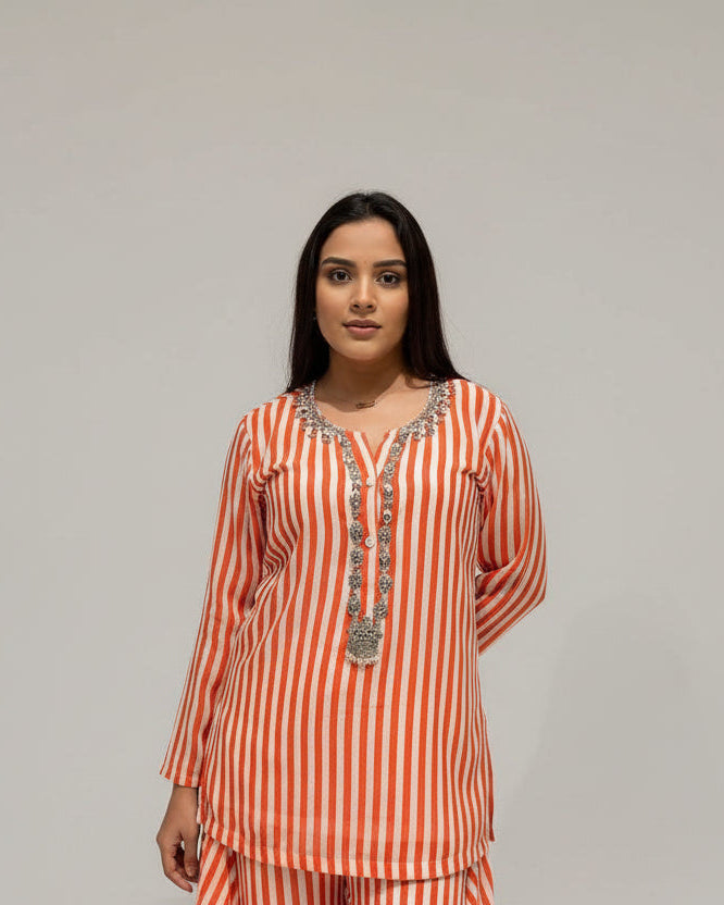 Woman wearing a red and white striped outfit with a decorative necklace against a beige wall.