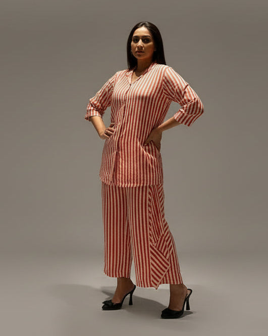 Person wearing a red and white striped dress standing in front of a decorative wall panel.