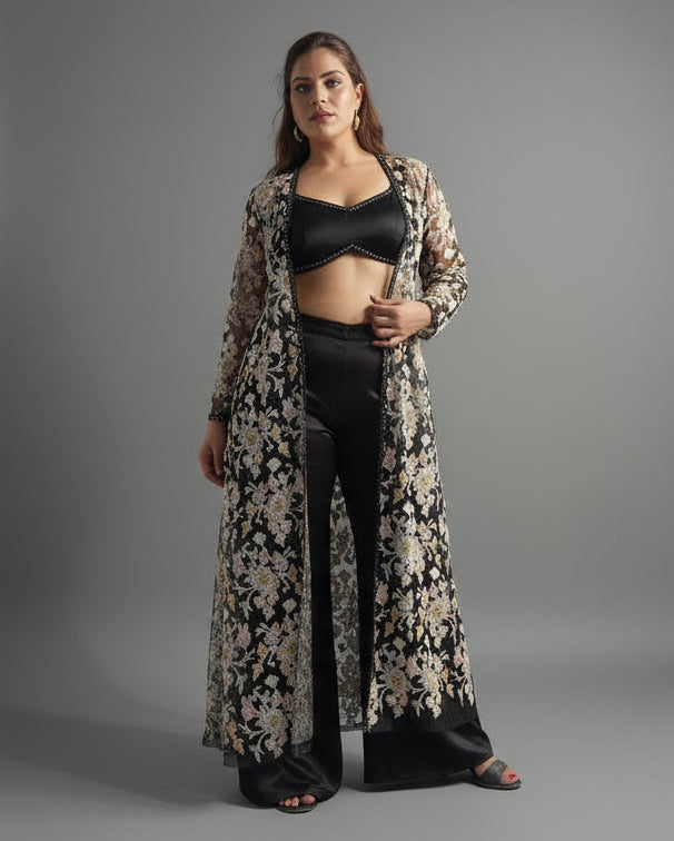 Woman wearing a long floral dress over a black top and pants on a gray background