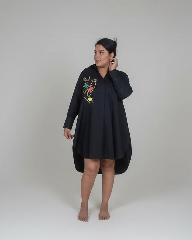 Person wearing a black dress with colorful embroidery on a white background