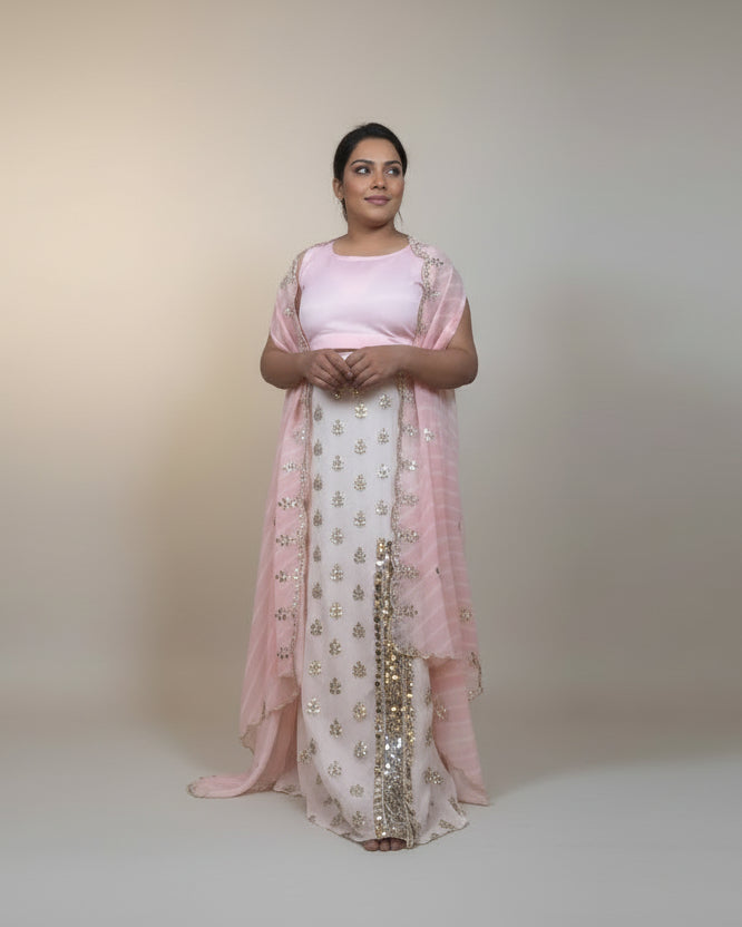 Woman in a pink and white traditional outfit standing in a room with beige walls and tiled floor.