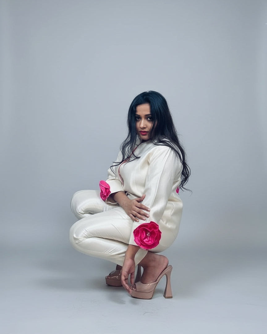 Woman in a white outfit with pink flowers posing indoors.